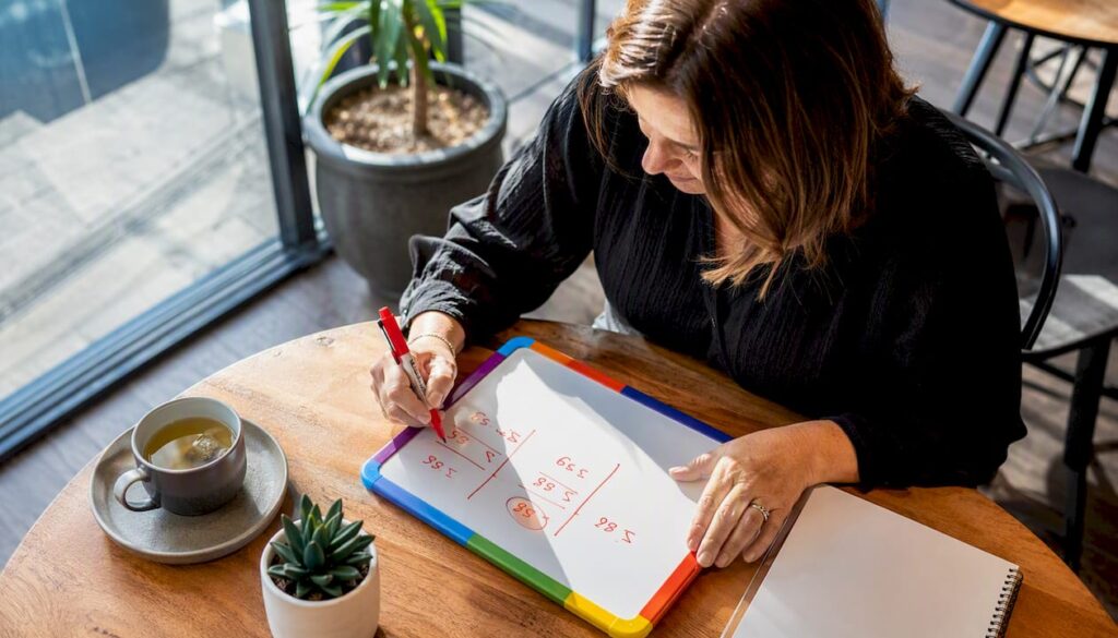 Hands writing pricing calculations on whiteboard